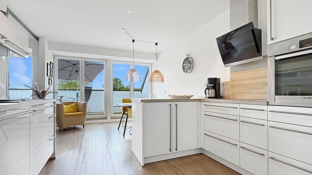A modern kitchen with white cabinets, a built-in oven, and a large window overlooking a balcony. - 3002 - Grömitz - Wohnung 3002 am Schoor in Grömitz (Grömitz)