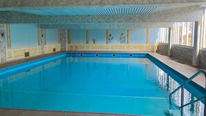 An indoor swimming pool with clear blue water, tiled floor, and a ceiling with a grid pattern. - 3002 - Grömitz - Wohnung 3002 am Schoor in Grömitz (Grömitz)