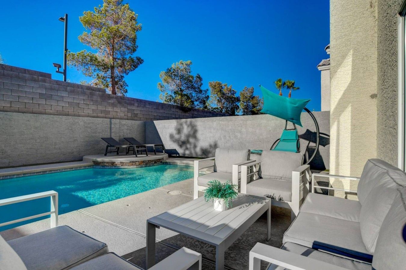 Un espace aménagé au bord de la piscine, avec une piscine à l’eau d’un bleu limpide, des chaises longues, une table et une plante en pot.