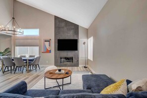 Una sala moderna con una televisión de pantalla plana, una chimenea, un comedor con sillas y un sofá con cojines.