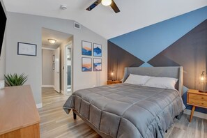 A bedroom with a bed, bedside tables, a desk, and a plant.