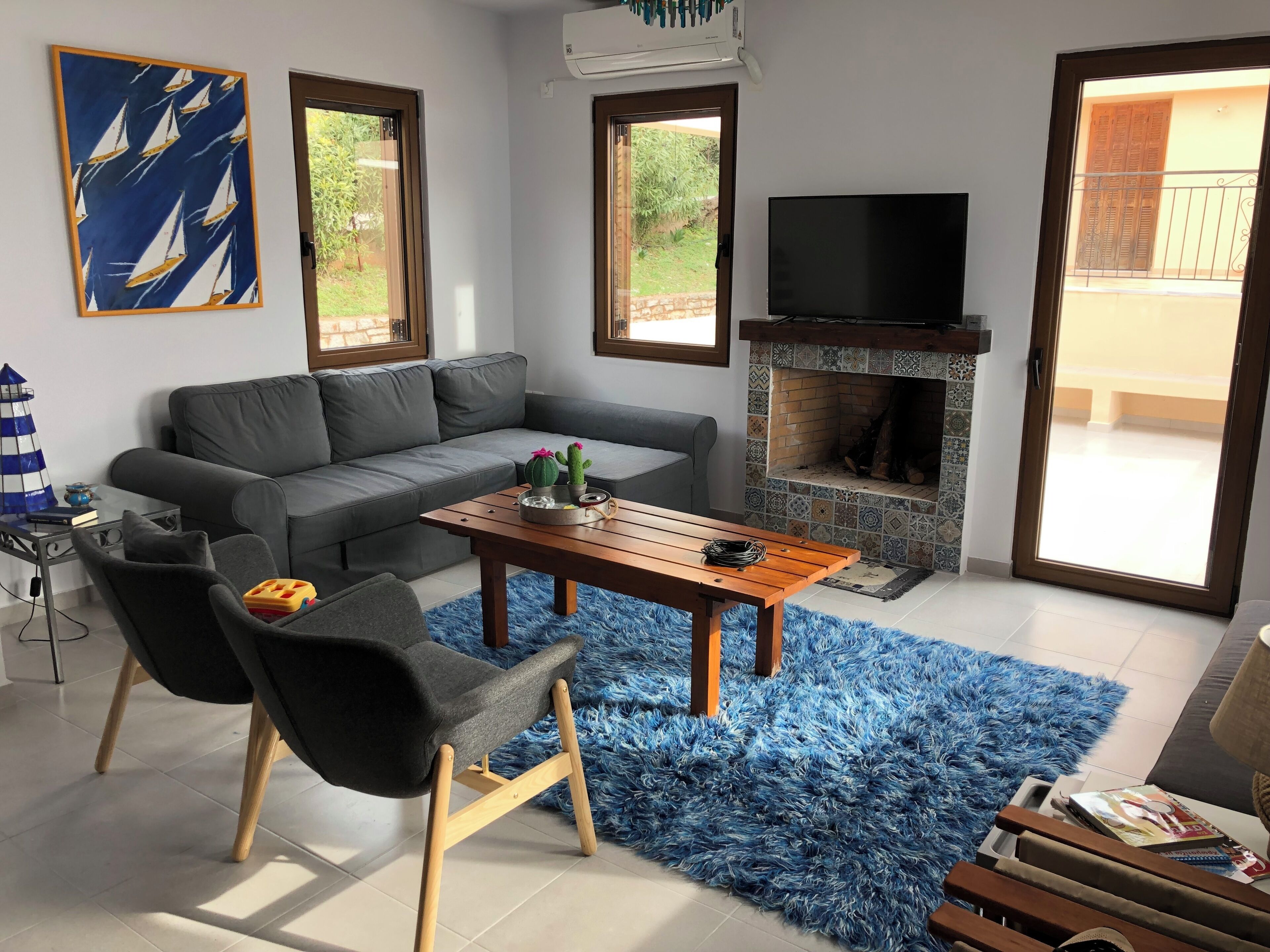 Een moderne woonkamer met een grijze bank, een houten salontafel, een blauw pluchen vloerkleed, een televisie en een open haard.