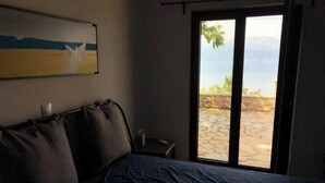 Une chambre à coucher comprenant un lit, une table de chevet, un tableau et une vue sur un patio extérieur, accessible par une porte coulissante.
