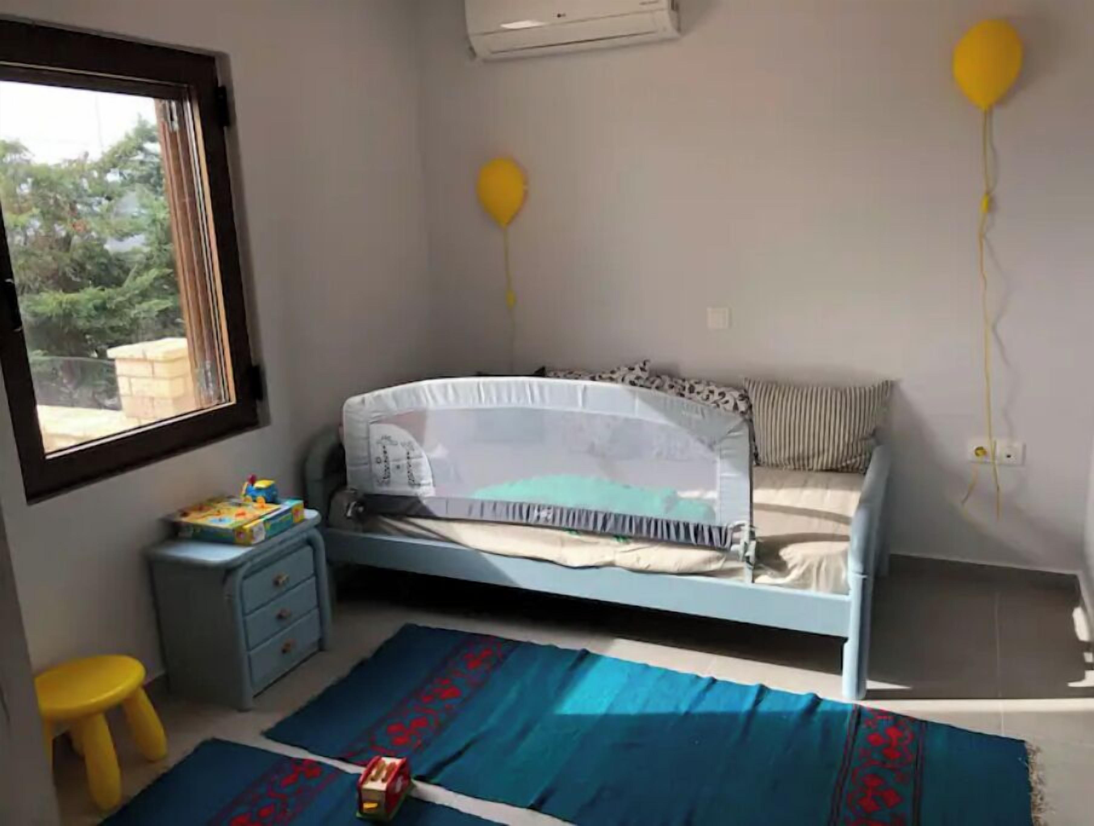Ein Schlafzimmer mit Bett, Fenster, einem kleinen Hocker und einem Spielzeug auf dem Boden.