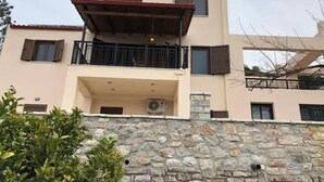 Un bâtiment à deux étages doté d’une façade en pierre, d’un balcon avec une rambarde en métal et d’un appareil de climatisation.