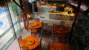 A restaurant with wooden tables and chairs, a bar area, and a view of the outdoor patio. - Villa Éden  (Santarém)