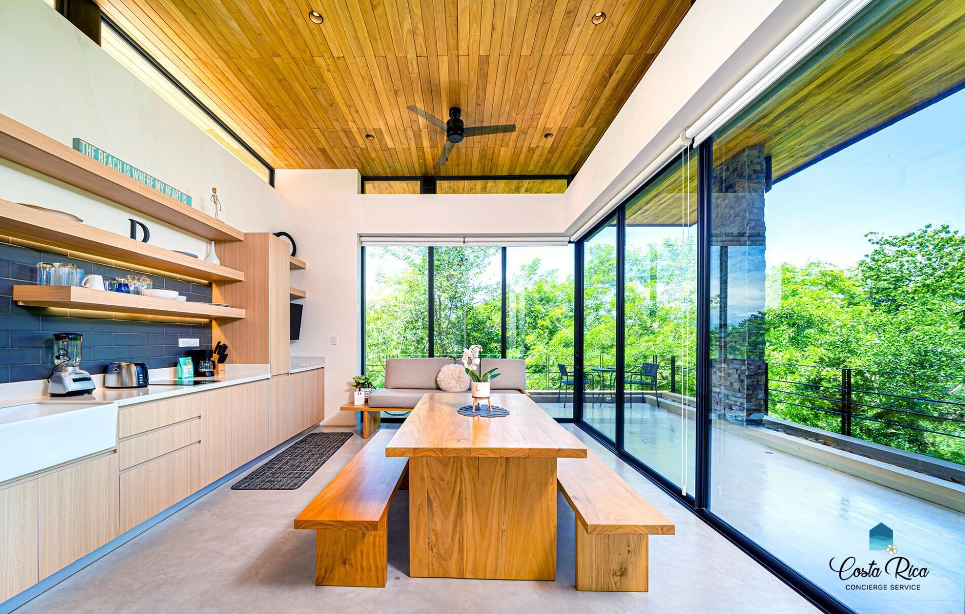Una cocina moderna con armarios de madera, un comedor con mesa de madera y ventanas amplias con vistas a zonas verdes.