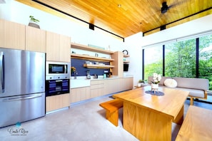 Een moderne keuken met houten kastjes, roestvrijstalen apparatuur en een groot raam met uitzicht op groen.