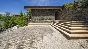 Un edificio moderno con fachada de piedra y techo plano, rodeado de un jardín ajardinado con escalones que conducen a la entrada.