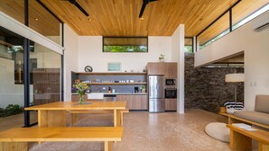 Una cocina moderna con horno empotrado, refrigerador y microondas. Hay una mesa de comedor de madera con bancos y un sofá con cojín.