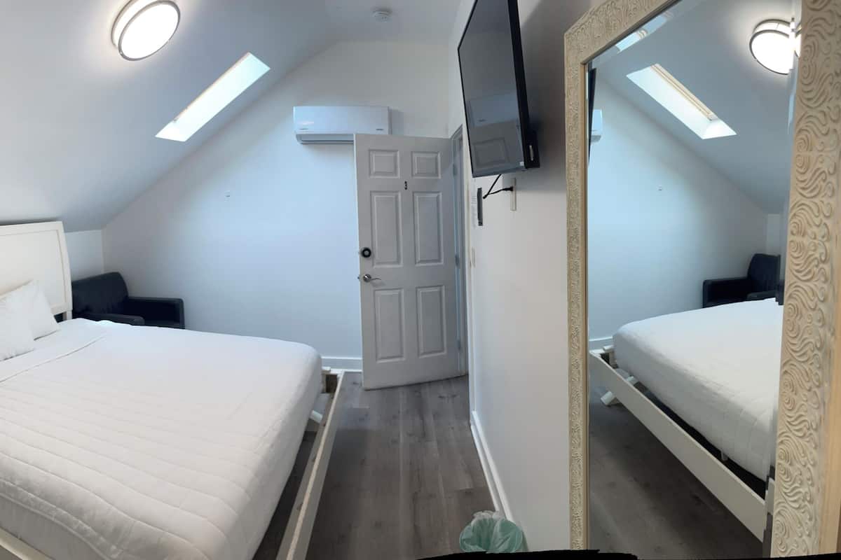 Une chambre à coucher avec un lit, une table de chevet, une commode, une porte et un miroir.
