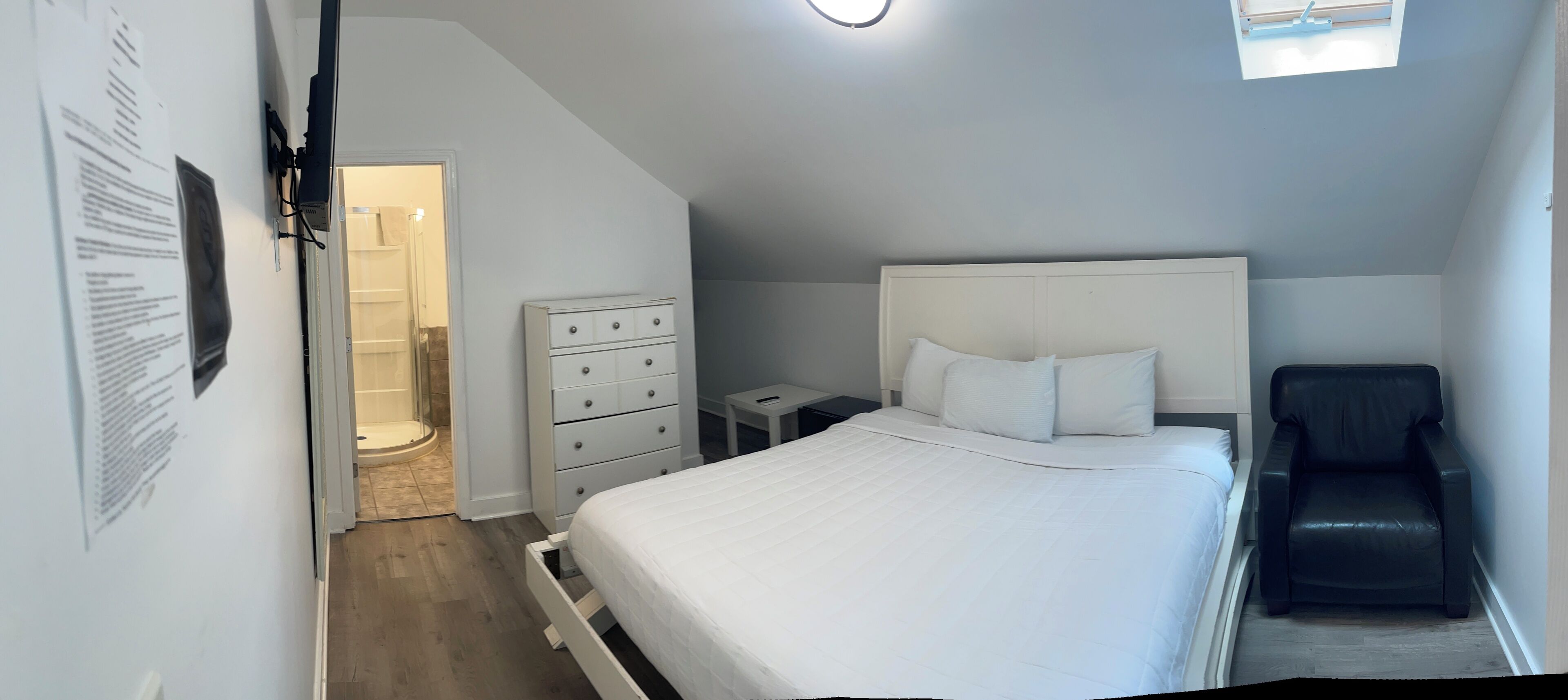 Un dormitorio con cama, cómoda, silla y tragaluz.