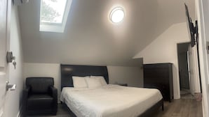Une chambre à coucher avec un lit, une chaise, une commode et une lucarne.