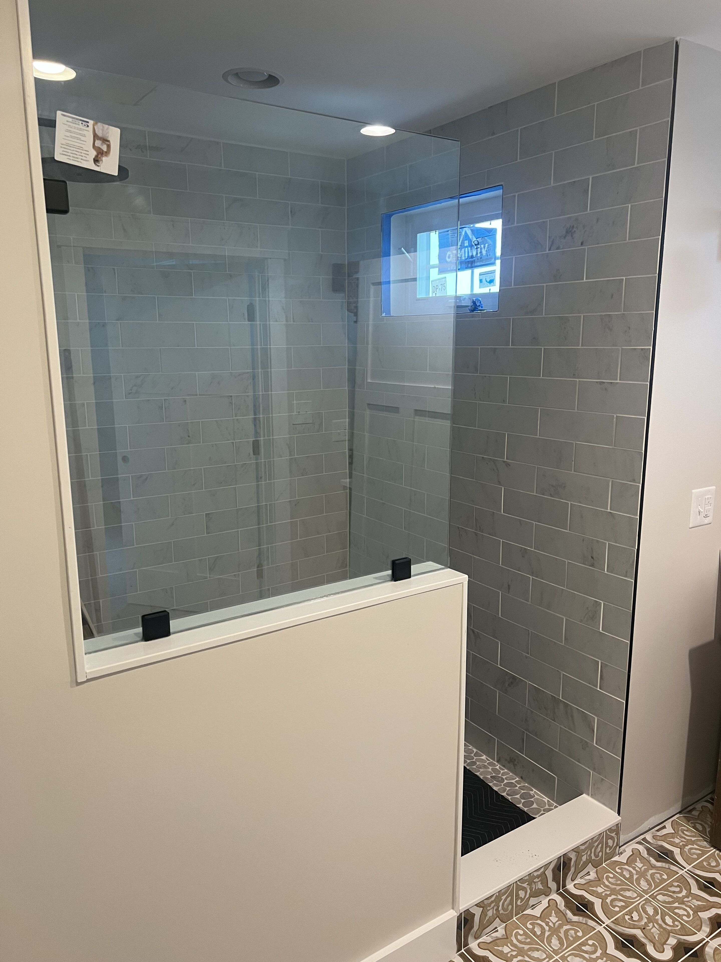 A modern bathroom with grey tiled walls, a glass shower enclosure, and patterned floor tiles.