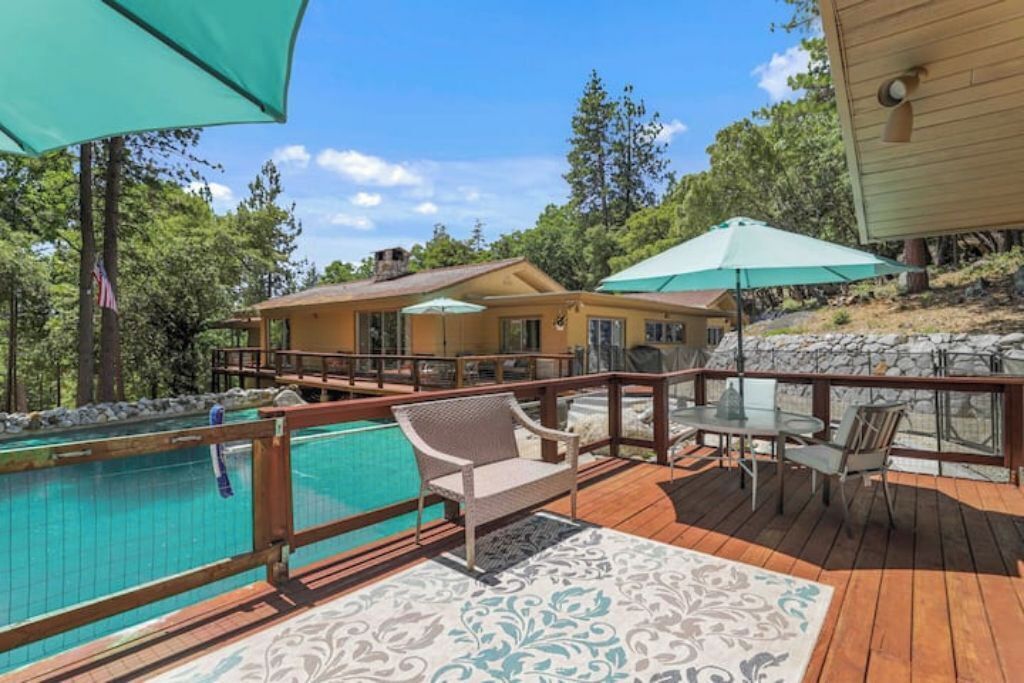 Eine Holzterrasse mit Pool, Gartenmöbeln und einem überdachten Bereich mit Sonnenschirmen.