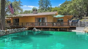 Una casa de dos pisos con piscina, terraza y pared de piedra.