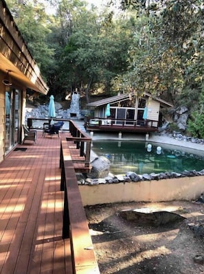 A wooden deck with outdoor seating, a small pool, and a rustic cabin-like structure surrounded by trees.