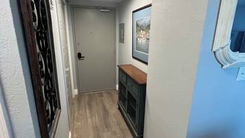 Un couloir étroit au plancher en bois, une porte au fond et un tableau encadré au mur.