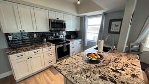 A modern kitchen with white cabinets, black backsplash, granite countertops, and stainless steel appliances. - 1/1 Ocean View Condo at Sandpiper. Watch rocket launches from the balcony! (Satellite Beach)