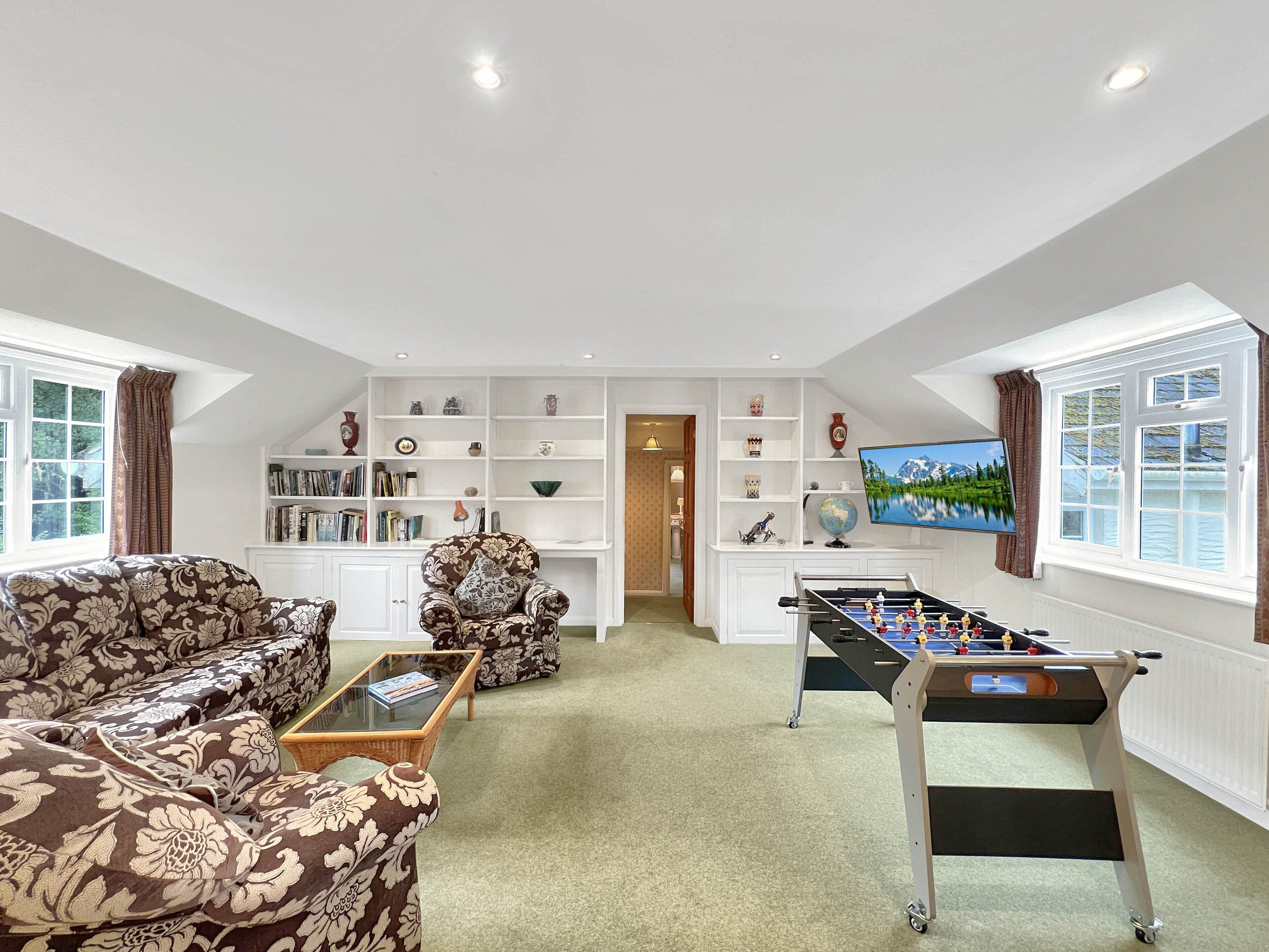 A spacious living room with a sofa set, a foosball table, a bookshelf, and a television.
