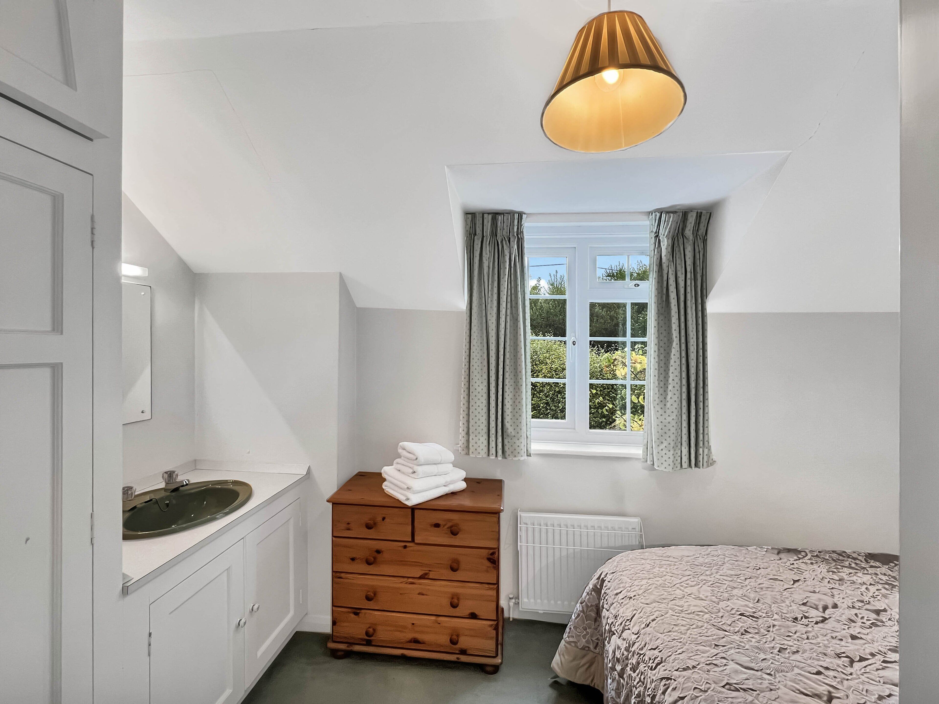 Una camera da letto con un letto, una cassettiera, una finestra con tende, un termosifone e una lampada a soffitto.