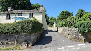 A narrow street with a white building on the left, a stone wall on the right, and a blue umbrella on the building. - Wey House near Withypool (Withypool)