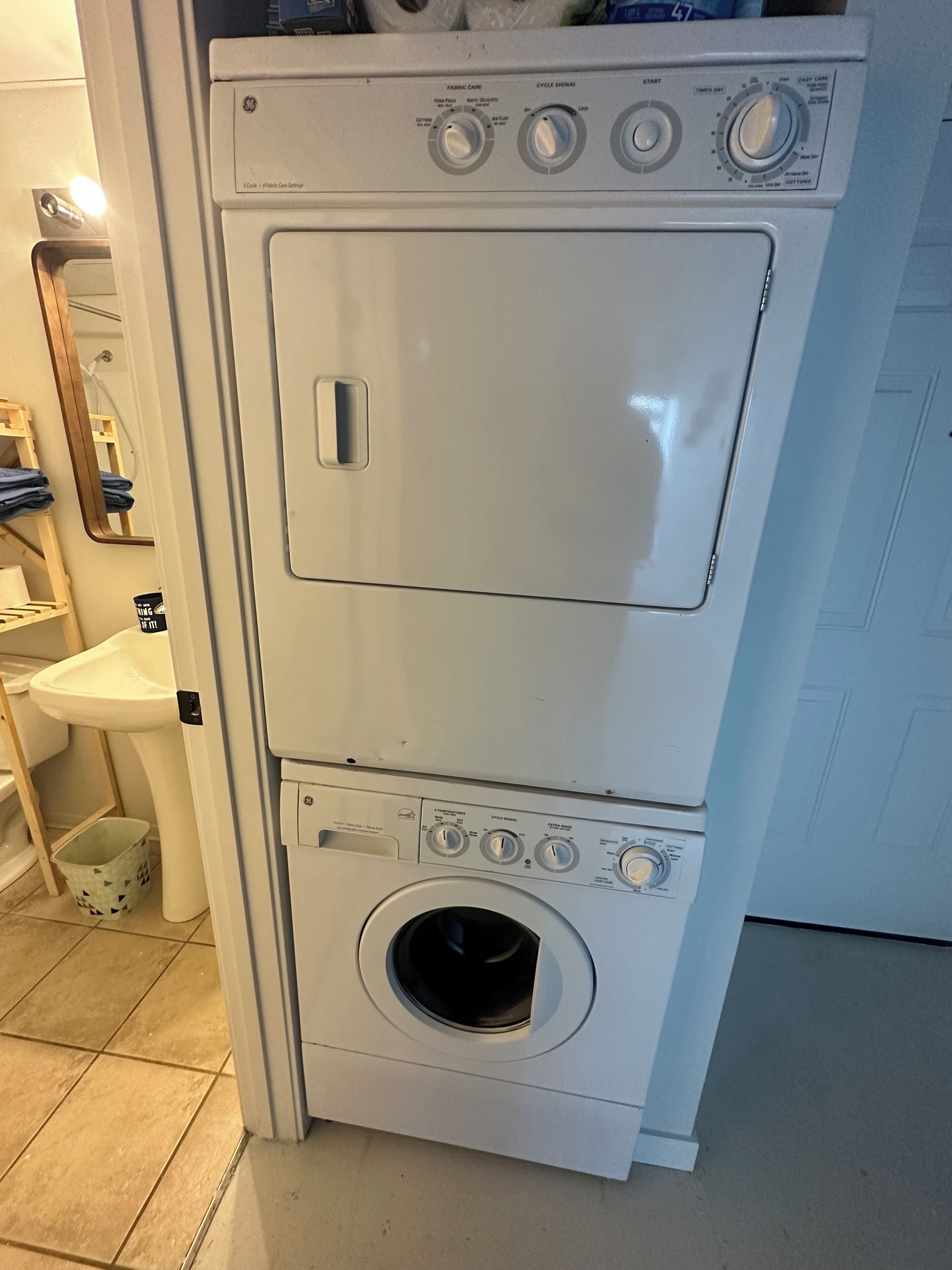 A compact, white, two-door washer and dryer unit with control knobs and a small window on the top door.