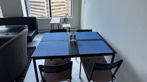 Ett modernt vardagsrum med ett matbord, två stolar, en soffa och ett stort fönster med utsikt över staden.