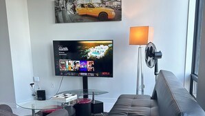 Ett modernt vardagsrum med en platt-TV som visar ett program, ett soffbord i glas, en svart lädersoffa och en lampa.