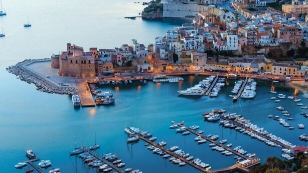 A coastal town with a historic fort, marina with boats, and buildings along the waterfront.
