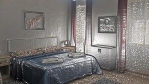 A bedroom with a bed, a nightstand, a lamp, a TV, and a door with a textured wall.