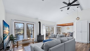 A spacious living room with a gray sectional sofa, a large flat-screen TV, and a black wood-burning stove.
