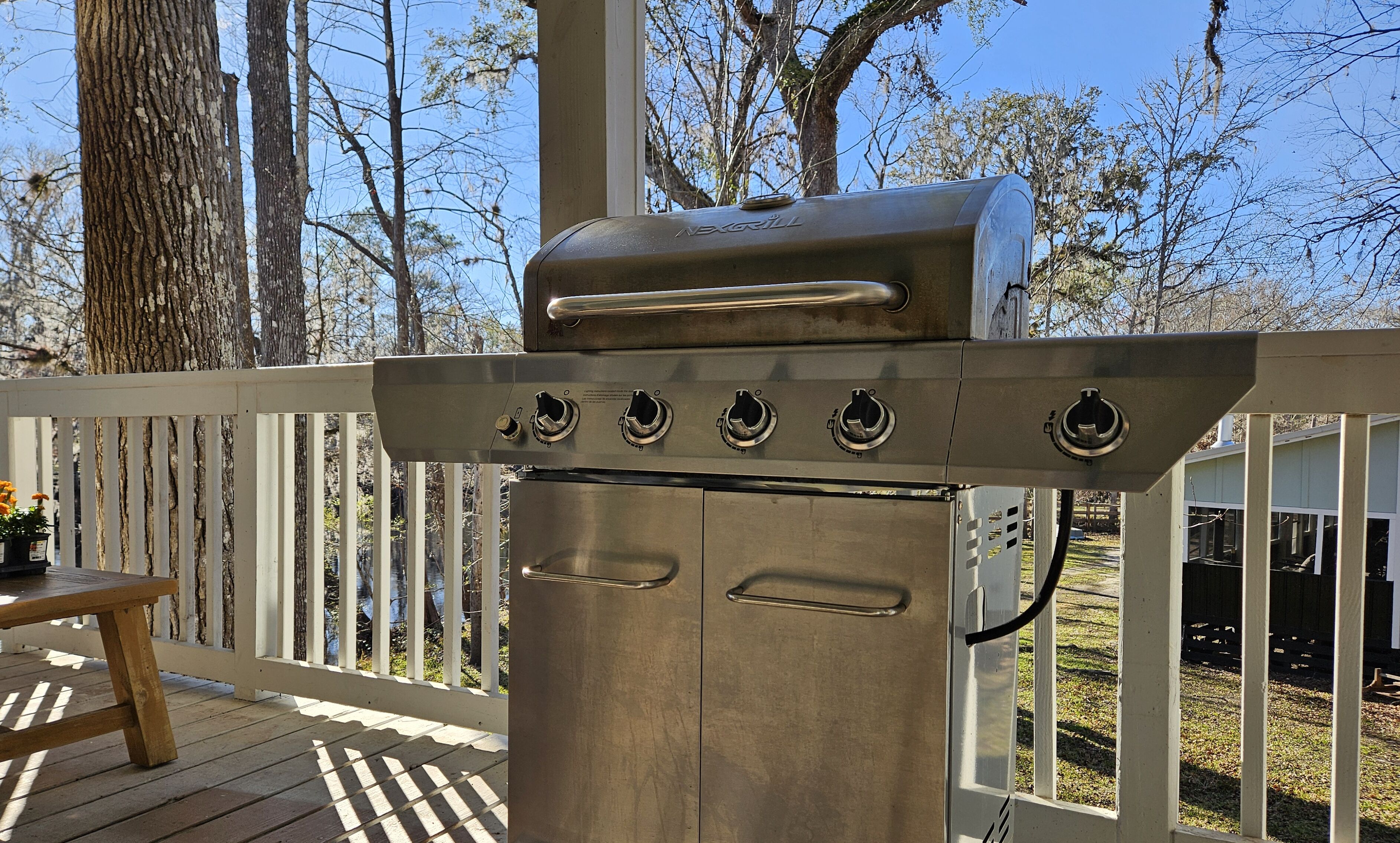 A stainless steel grill with four burners, a control panel, and a handle, located on a wooden deck with a white railing.