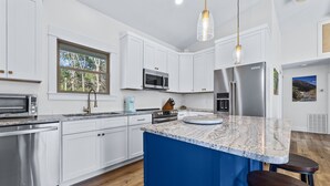 A modern kitchen with white cabinets, stainless steel appliances, a blue island, and a hanging pendant light.