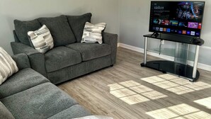 Een moderne woonkamer met een grijze bank, een glazen salontafel en een flatscreen-tv met een streamingdienst interface.