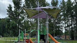 Een speeltuin met glijbanen en klimconstructies, omringd door een hek en bomen.