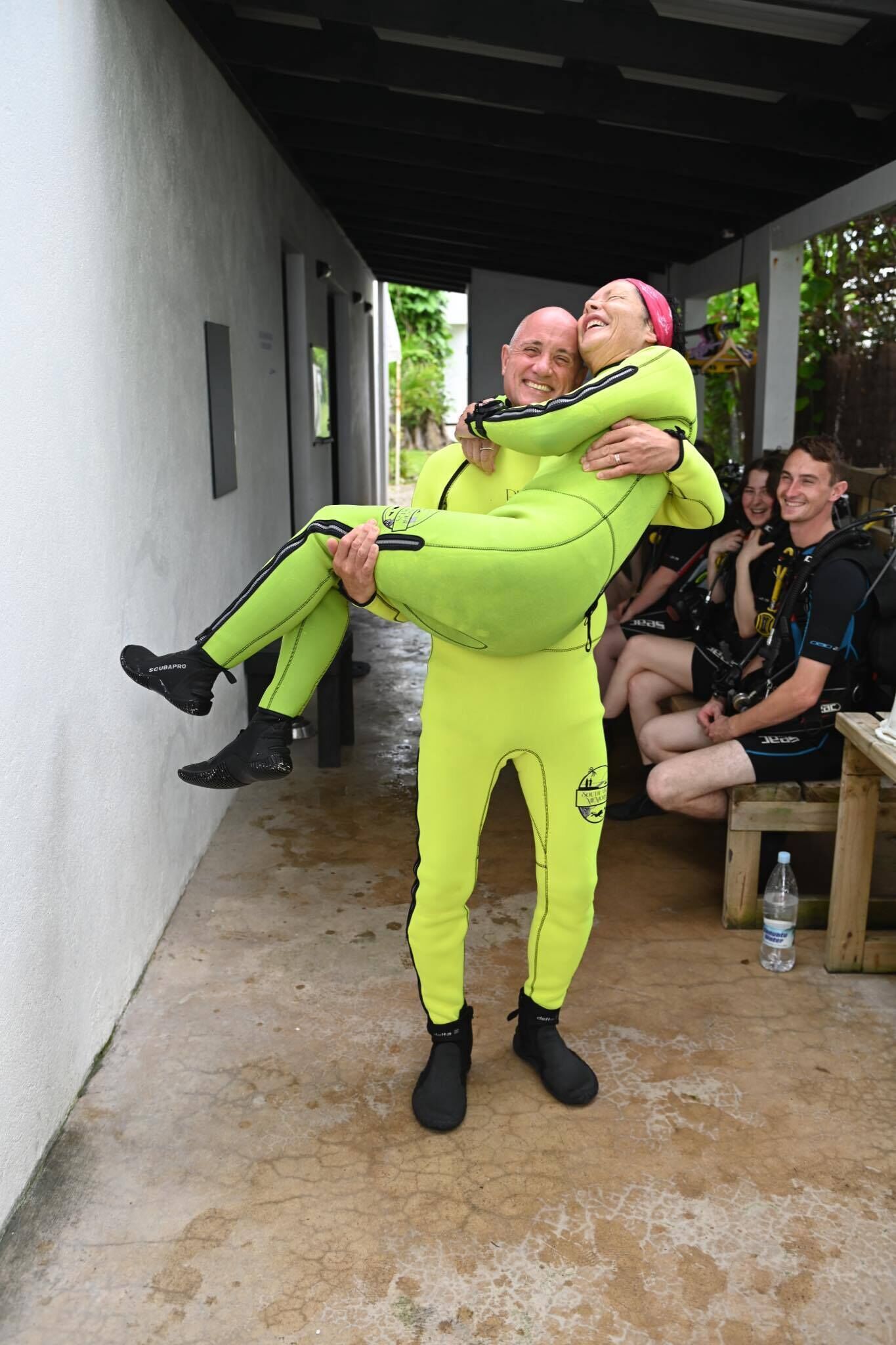 Una persona con un traje de neopreno amarillo brillante siendo llevada por otra persona.