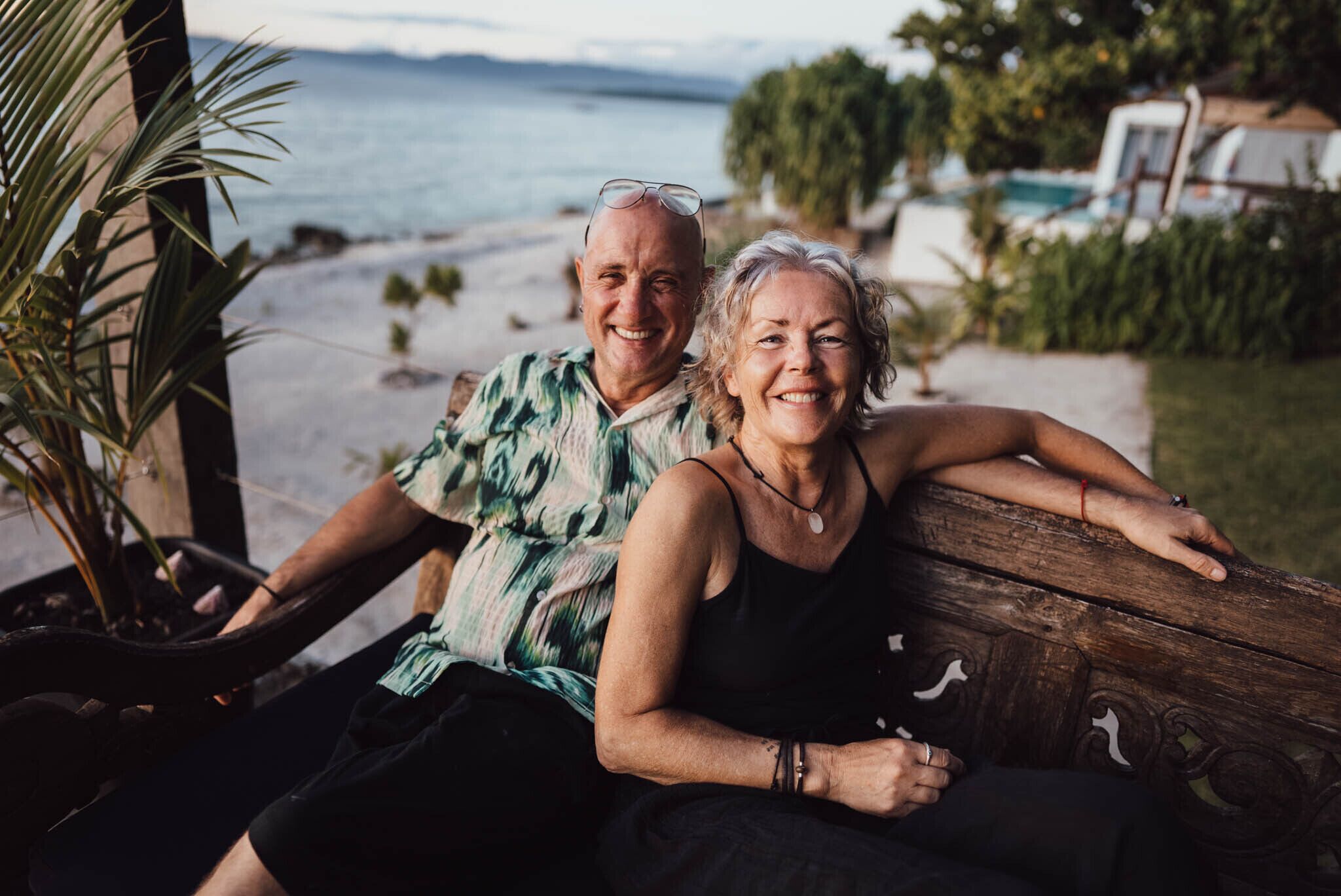 A couple sitting on a wooden bench with a view of a beach and ocean.