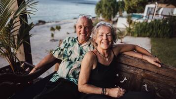 A couple sitting on a wooden bench with a view of a beach and ocean.