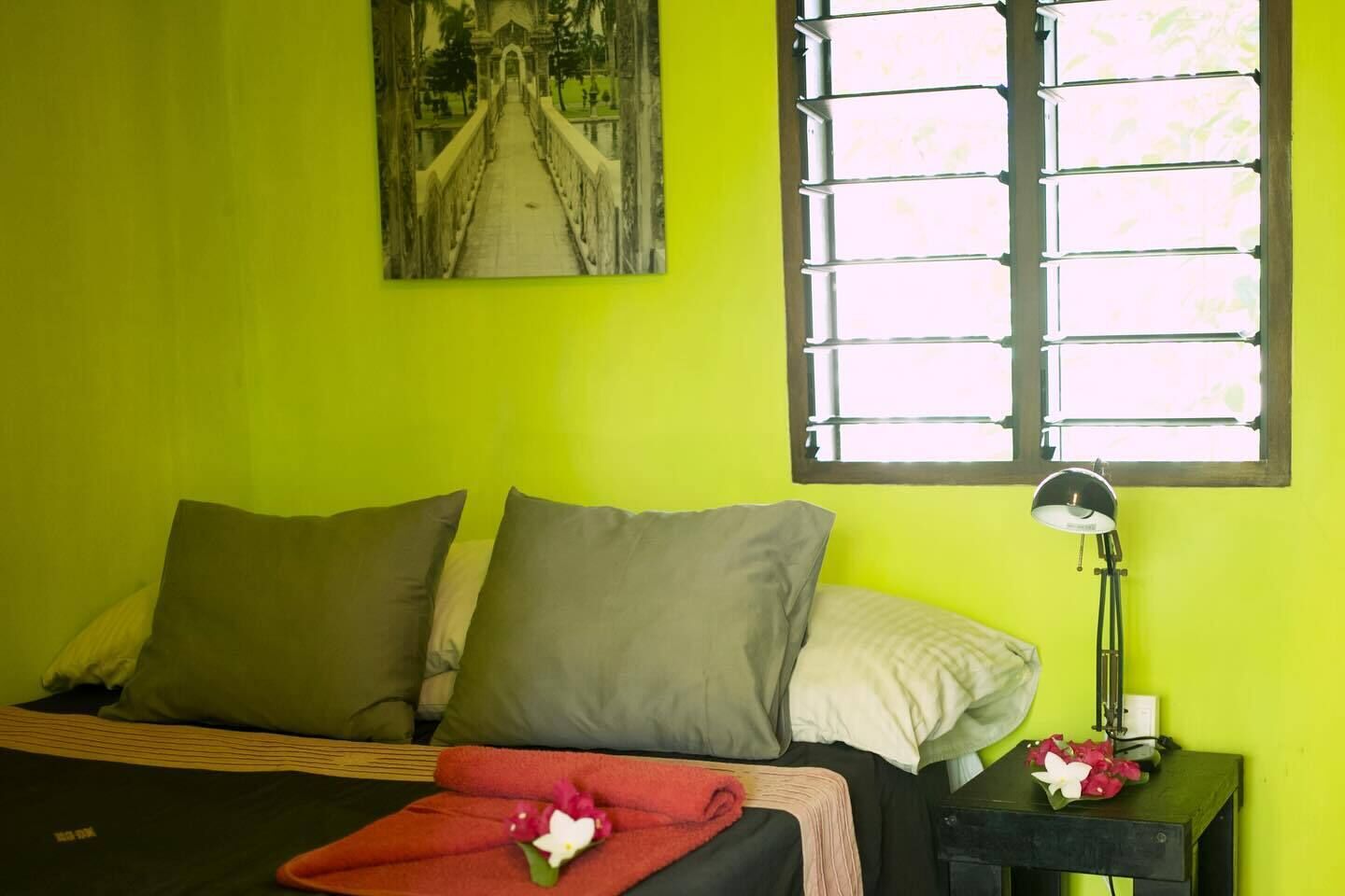 Une chambre à coucher avec un lit, des oreillers, une table de chevet avec une lampe et une fenêtre avec des stores.