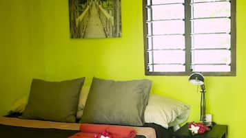 Une chambre à coucher avec un lit, des oreillers, une table de chevet avec une lampe et une fenêtre avec des stores.