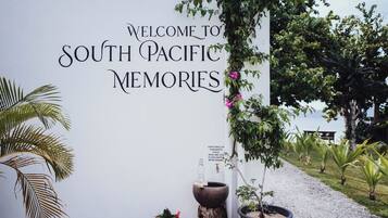 Un cartello di benvenuto per South Pacific Memories, con un vialetto fiorito e piante in vaso.