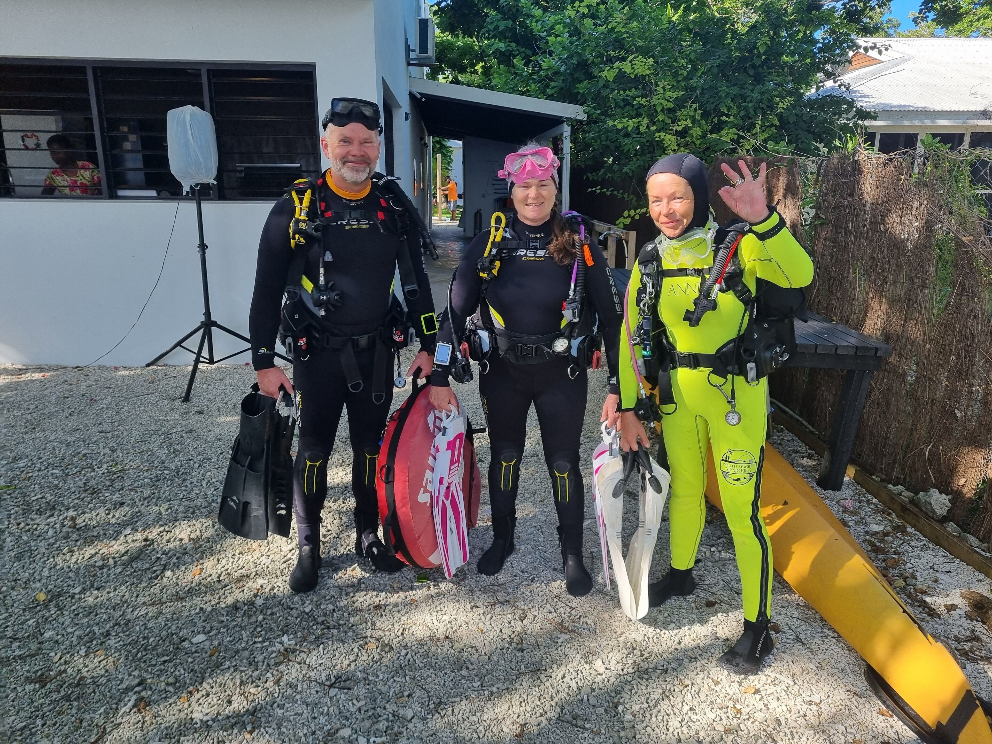 Three individuals in scuba diving gear standing outdoors.