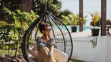 A person sitting in a hanging chair in a garden area with a pool in the background.