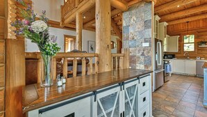 A rustic kitchen with wooden beams, stone accents, and a central island with a vase of flowers. - Eagle's Nest CITQ 271666 (Mont-Blanc)