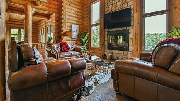 A log cabin interior with a stone fireplace, leather sofas, and large windows. - Eagle's Nest CITQ 271666 (Mont-Blanc)