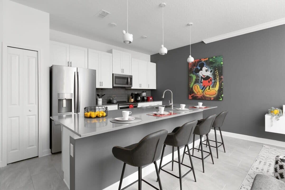A modern kitchen with white cabinets, a stainless steel refrigerator, a microwave, and a large island with bar stools.