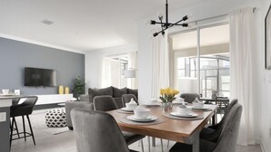 A modern dining area with a wooden table set for four, grey upholstered chairs, and a large window with white curtains. - Charming Mickey-Themed Home, Prime Location (Kissimmee)