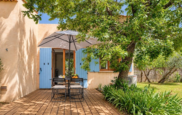 A patio with a table and chairs, an umbrella, and a tree providing shade.