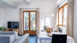 A room with a TV, grey sofa, dining table with fruit, and large windows. - Air-conditioned flat for 4 people with garden - Golfe de St-Tropez (Le Plan-de-la-Tour)